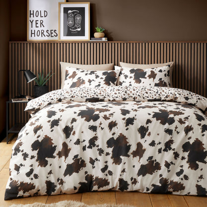 Cow print bedding set on a bed with a wooden headboard and decor items.